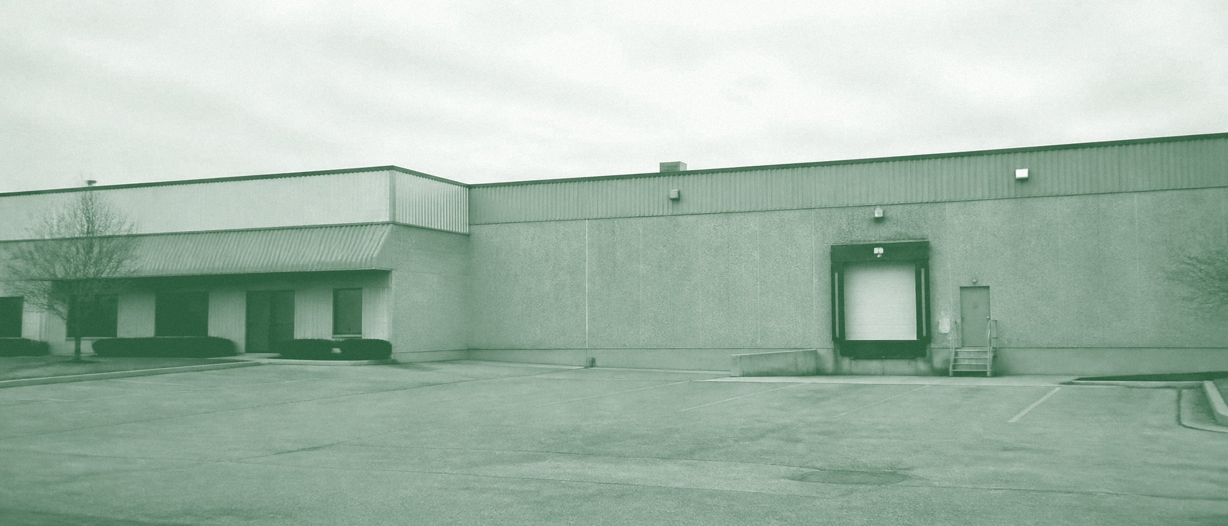 A plain single-story industrial flex building with a loading dock and empty parking lot
