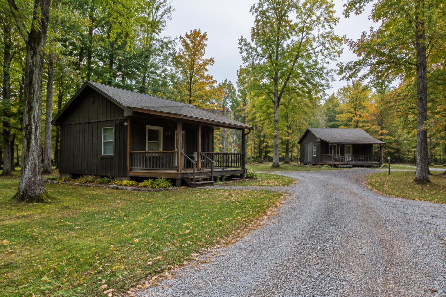 Two modest cabins beside a gravel drive in a wooded Midwest setting